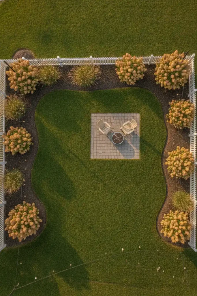 Overhead view of a backyard lawn split into open grass, curved beds, and a small gravel seating corner