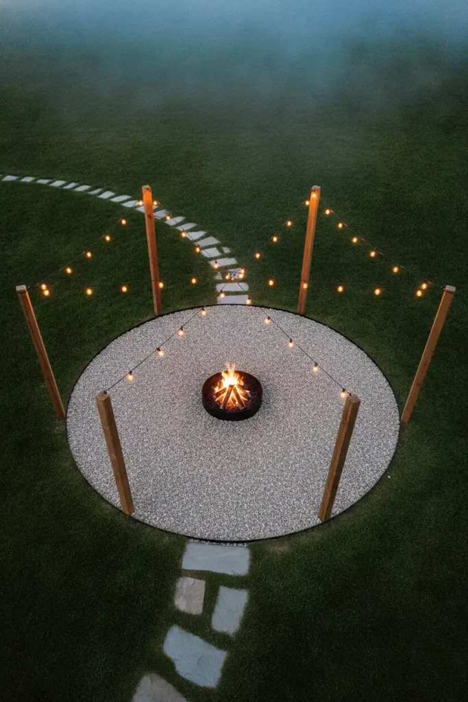 Rustic backyard fire pit with a pea gravel floor, flagstone path and café lights on cedar posts